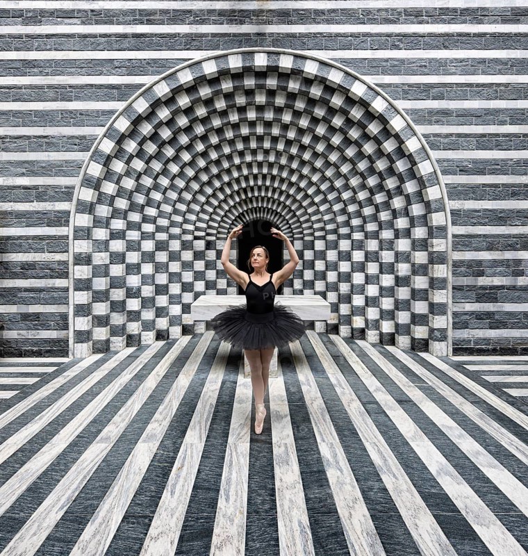 Ballerina in a black tutu poses in front of modern, stripe-patterned, symmetrical granite architecture, San Giovanni Battista, Mogno, Ticino, Switzerland