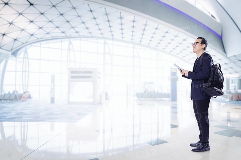 Junger Geschäftsmann mit digitalem Pad lächelnd glücklich im Flughafen warten Halle