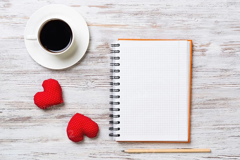 Coffee cup notepad pencil and two red hearts on wooden surface
