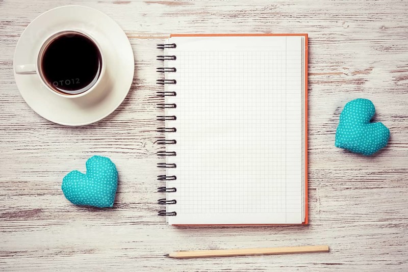 Coffee cup notepad pencil and two hearts on wooden surface