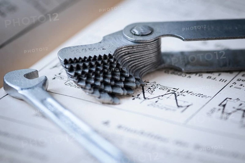 Detailed view of a fanned-out thread gauge with a small spanner lying next to it on an old technical drawing