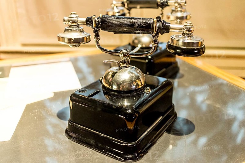 An antique analog telephone set with black box base and golden ringer, and handset