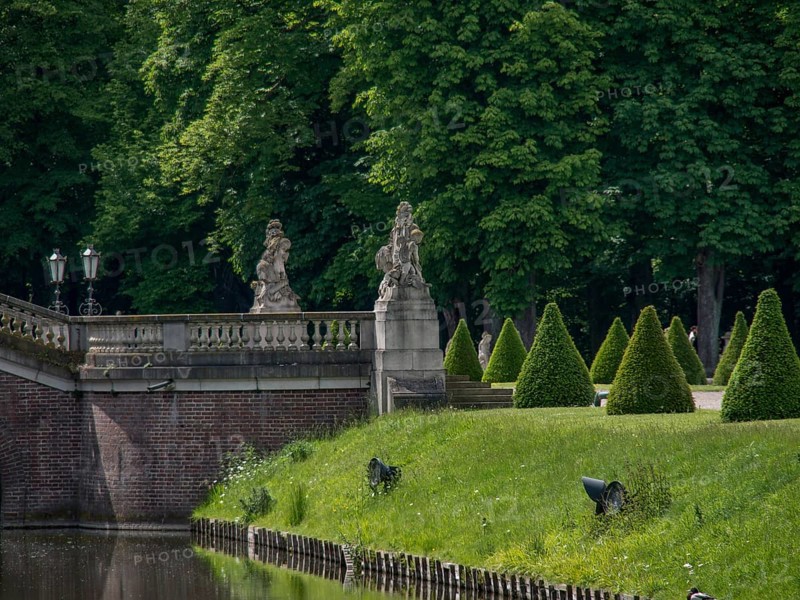 A stone bridge with statues leads over a river, flanked by neat hedges and lush trees, nordkirchen, münsterland, germany