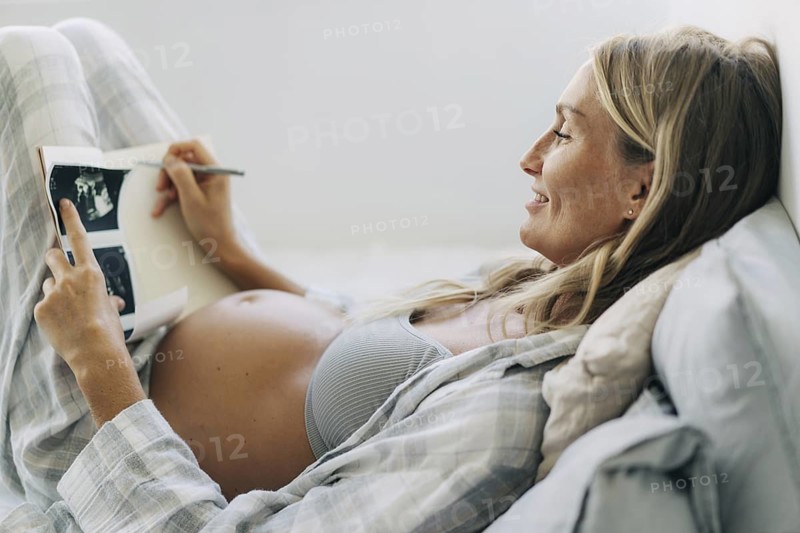 Eine schwangere Frau macht sich in einem Notizbuch Notizen über das Ultraschallergebnis
