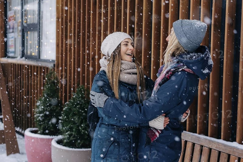 Erwachsene Freundinnen, die sich umarmen und lachen und sich über das verschneite, kalte Wetter freuen
