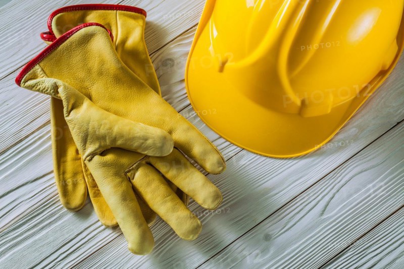 Yellow leather work gloves and construction helmet on old white lacquered wooden panels
