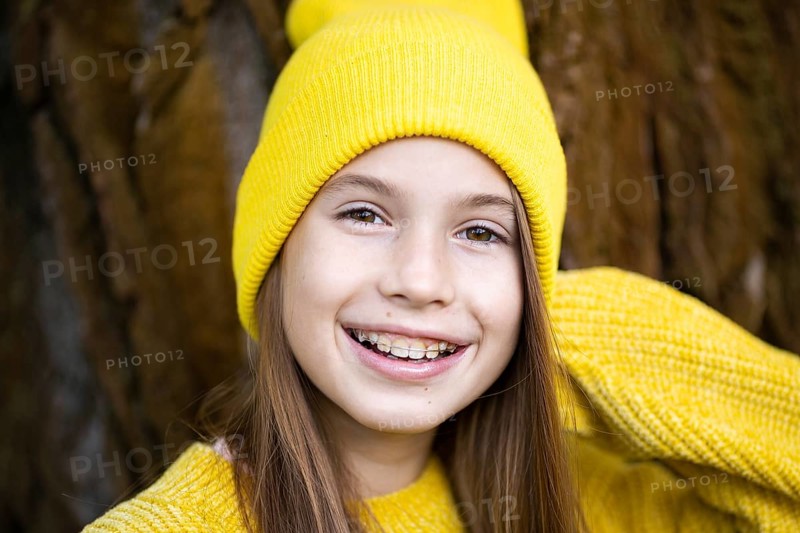 Cute and happy teenage girl with braces smiling at camera in yellow clothes in park. Concept of dentist and orthodontist. Pretty teenage girl wearing teeth appliance smiling happily outdoors