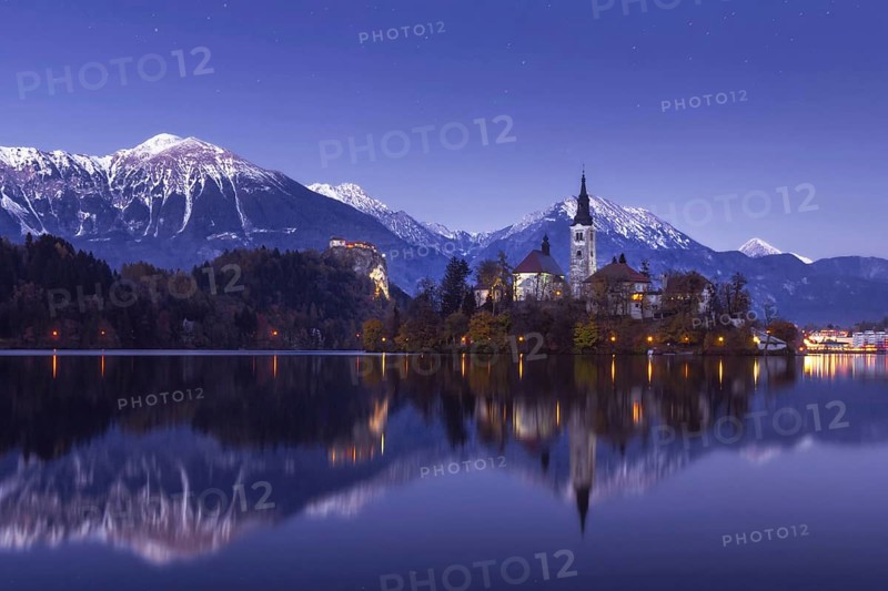 Scenic view of lake Bled at winter night with castle rock and St Martin church under beautiful starry sky reflected in lake water