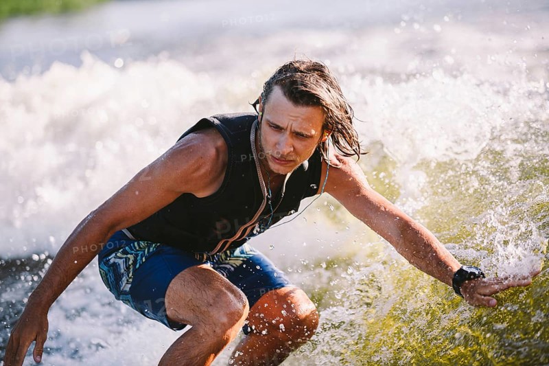 Active wakesurfer jumping on wake board down the river waves. Surfer on wave. Male athlete training on wakesurf training. Active water sports in open air on board. A man catches a wave on surf