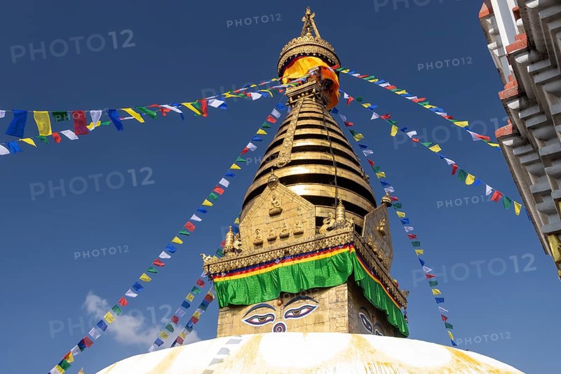 Swayambhunath, Swayambhu Mahachaitya, sometimes called the Monkey Temple, the Swayambhu stupa, one of the UNESCO World Heritage Sites of the Kathmandu Valley photographed in winter with the blue sky in the background. On the white dome stands a cubic part, the harmika, with eyes painted on its four sides, known as Eyes of Buddha or Wisdom Eyes. The golden spire is above it, and Buddhist prayer flags hang from the top. Kathmandu Metropolitan City, Bagmati Province, Nepal