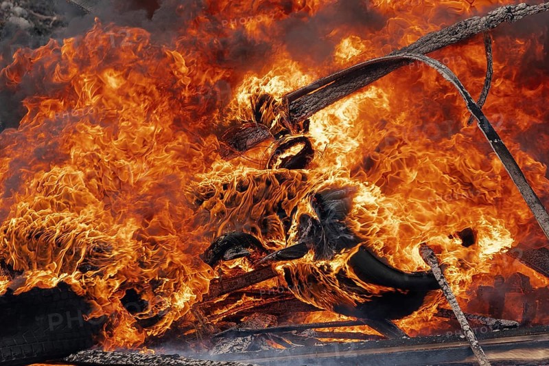 Burning cars wheels, strong flame of red-orange fire and clouds of black fumes. Selective focus, blur from strong fire