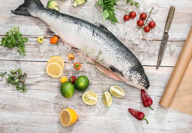 Raw salmon fish in ice and vegetables on white table. Baking paper