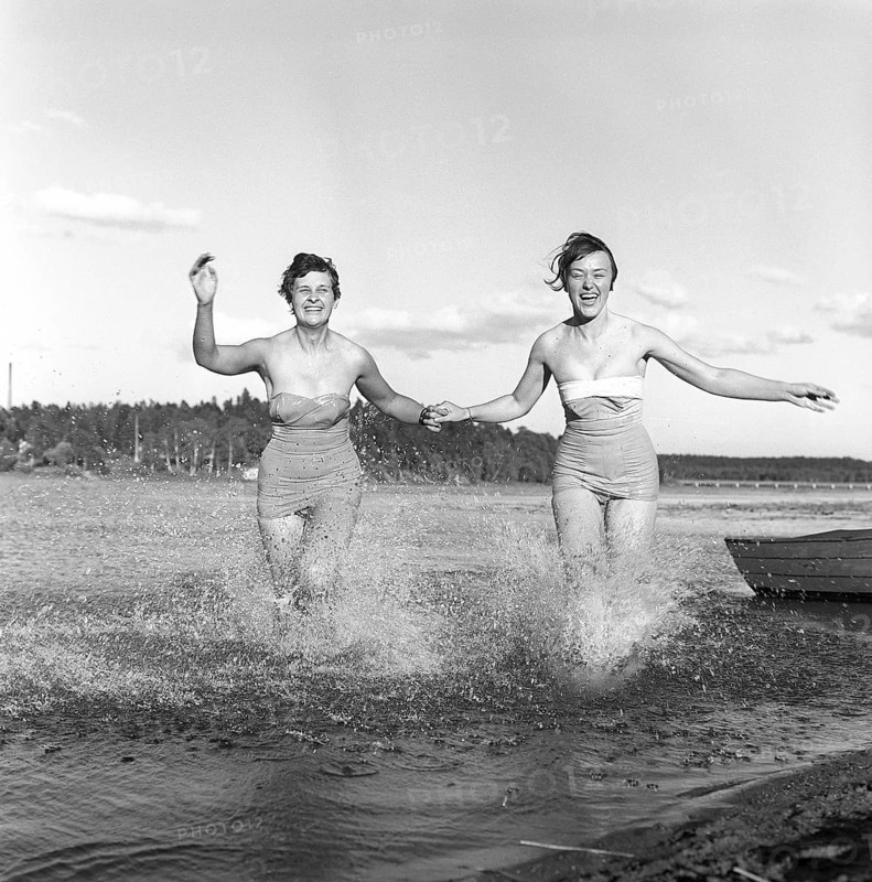 1950s summer. Two young women runs on the shallow part of the beach and the water splashes. Sweden 1959. Kristoffersson ref CG10-8