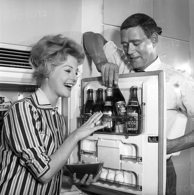 In the kitchen 1950s. A couple in their kitchen and at the refrigerator where the beer is kept in the door shelf. Five beer bottles are seen. Mrs is holding a bowl of shrimps. Sweden 1959. Kristoffersson ref CH77-3