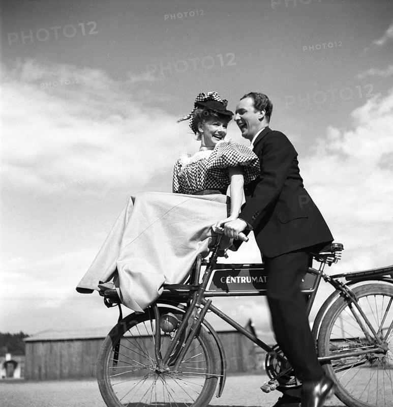 1940s couple on a bicycle. A young couple is riding their bicycles on a sunny day. They are both actors, Sonja Wigert and Arnold Sjöstrand and they have some fun while recording their new film. Sweden 1944. Photo Kristoffersson K23-6