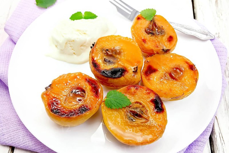 Five halves of quince baked with honey, ice cream and fork in a plate on a lilac napkin on a wooden plank background