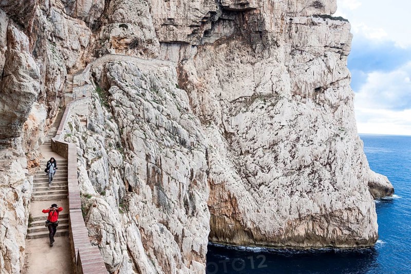 Two women walking on staircase amidst Capo Caccia cliffs. Alghero, Sardinia. Italy