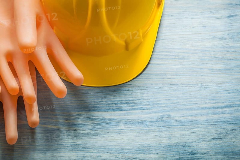 Pair of rubber insulating gloves building helmet on wooden board electricity concept