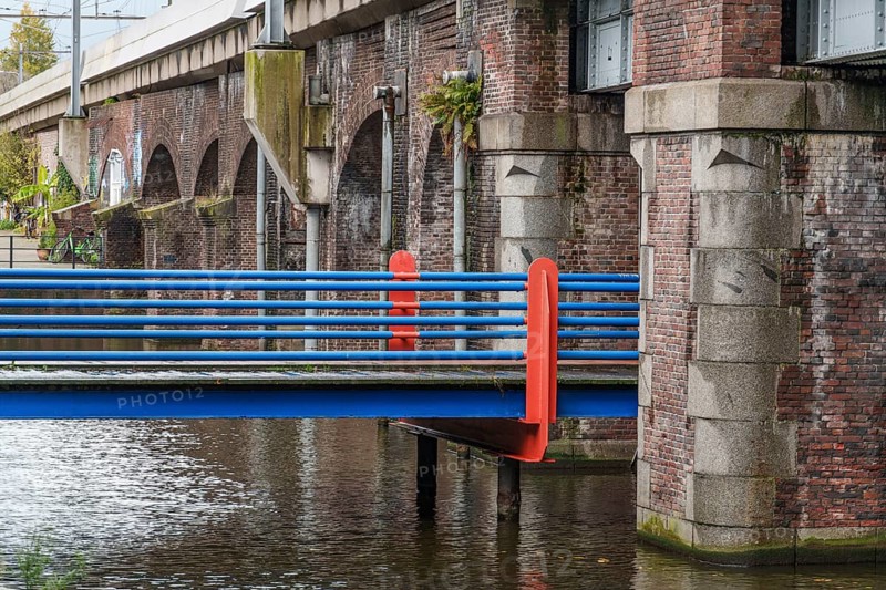 Brick bridge with blue-orange railings along a canal, Amsterdam, Netherlands