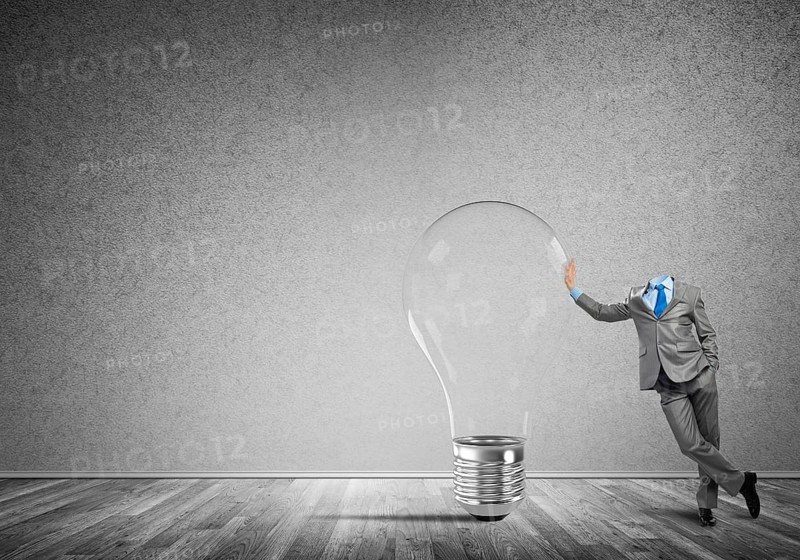 Headless businessman in empty room leaning on glass light bulb