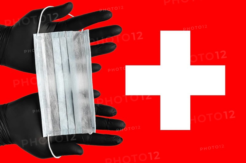 Doctor holds face mask in hands in black medical gloves on background colors flag of Switzerland. Concept coronavirus quarantine, pandemic outbreak, grippe, airborne diseases. Human respiratory mask