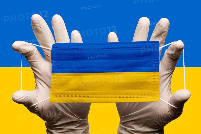 Doctor holding in white gloves protection medical face mask with National flag of Ukraine superimposed on mask. Concept coronavirus disease SARS-CoV-2 pandemic on background of National Ukrainian flag
