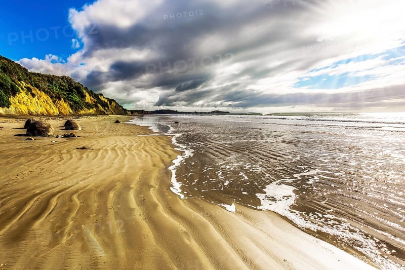 New Zealand. Moeraki's huge round boulders on a sandy beach. The Pacific ocean tide begins. The concept of ecological, exotic and phototourism