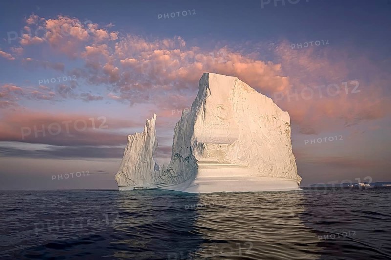 Large glaciers in the bay by the rocky shore in the light of the setting sun