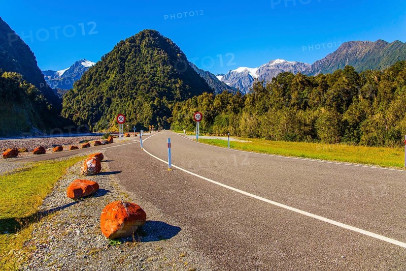 Snowy peaks of rocks are visible in the distance. Wonderful summer day. Great highway among fields, forests and hills. South Island of New Zealand. The concept of active and photo tourism