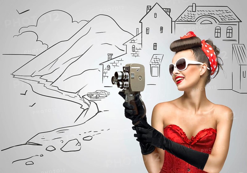 Glamorous pin up tourist girl filming a landscape with an old retro cinema 8mm camera, standing in front of a sketchy background