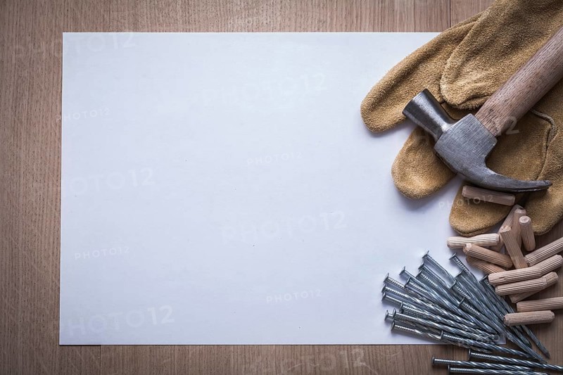 Clean sheet of paper steel nails claw hammer wooden dowel pins and leather safety gloves on wood board copyspace construction concept