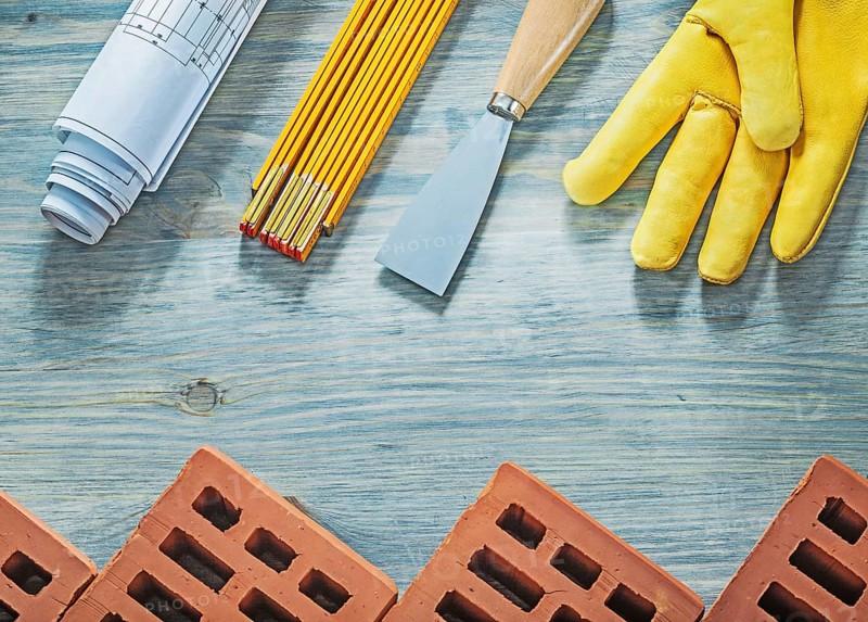 Assortment of red bricks safety gloves palette knife blueprints wooden meter building concept