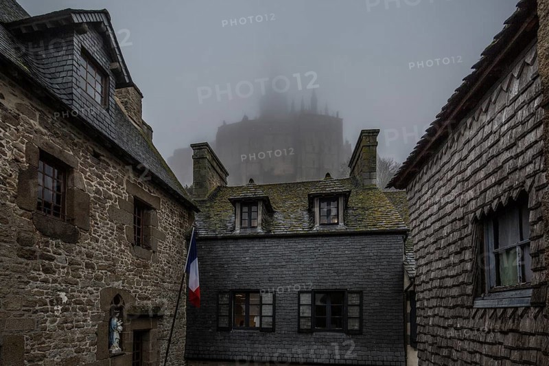 Mont-Saint-Michel, monastery hill, houses at the lower end of the Grande Rue above the abbey in the fog