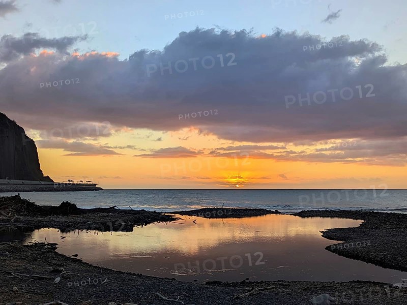 Sunset over the ocean, with striking reflections on wet sand and dramatic clouds in the sky. Saint-Denis, La Réunion