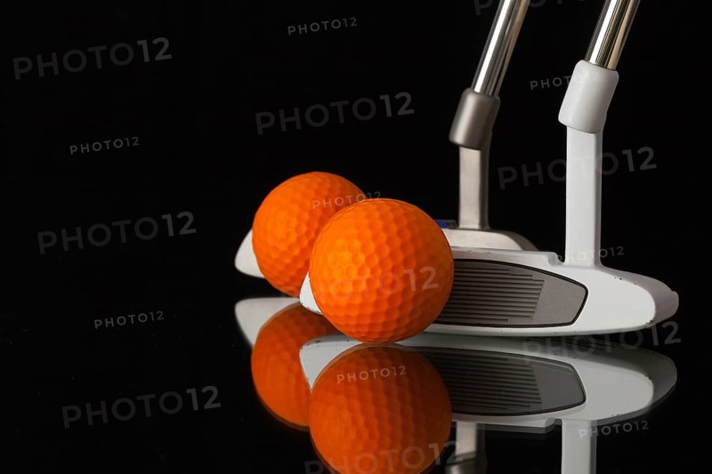 Two different golf putters and balls on a black glass desk