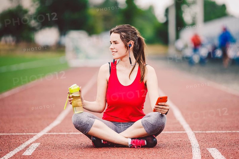 Beautiful fitneß girl uses smartphone at stadium after workout. Sports and healthy. Sport woman use of cellphone inside sport complex. Sport and technology. resting after workout, run at red track