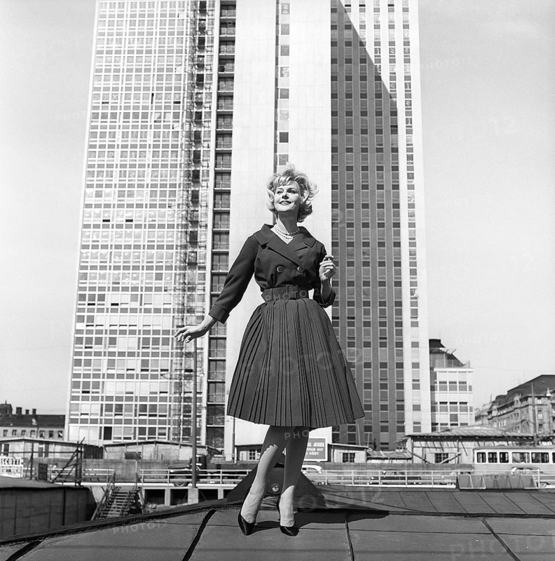 In the 1950s. A woman modelling a 1950s outfit with a jacket and skirt in matching dark. In the background the newly finished skyscraper housing the swedish tax offices. Sweden 1959 Kristoffersson ref CH21