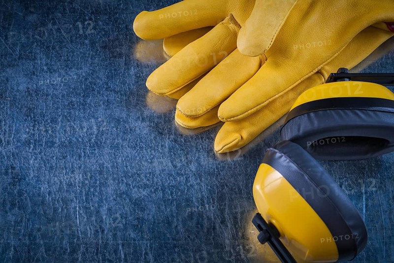 Noise reduction yellow headphones and leather protective gloves on scratched metallic background construction concept