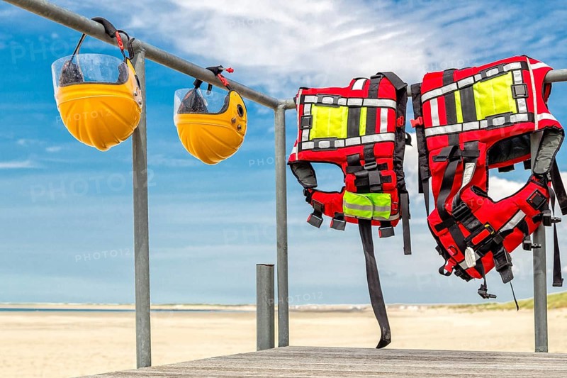 Safety helmets and life jackets hanging on railing near beach at coast