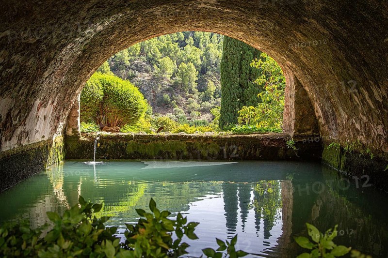 Tranquil, arched tunnel with views of water and trees in the background, Jardines de Alfabia gardens, Bunyola, Majorca, Spain