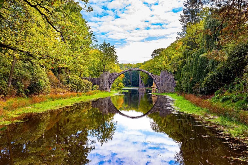 The Devil's Bridge on the Rakots River. Park Kromlau, Germany. The basalt columns of the bridge form a perfect circle with their reflection in the water. Picturesque narrow bridge in the park
