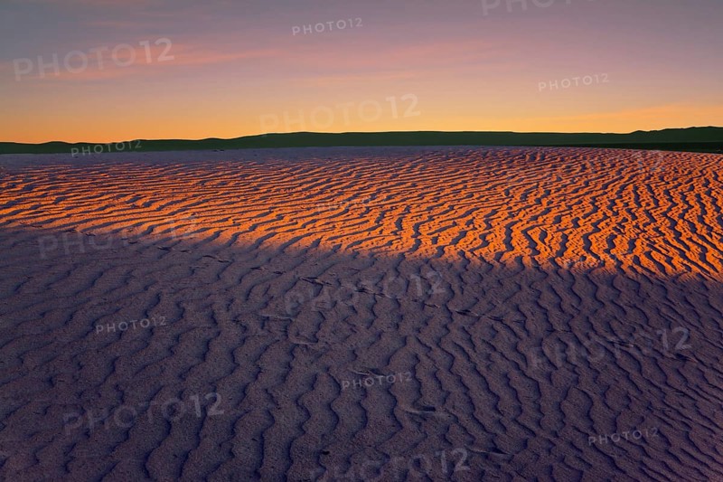Orange sunset in the desert. Mesquite Flat Sand Dunes, California. The gentle slopes of the sand dunes are rippled by the wind. Concept of active, ecological and photo tourism