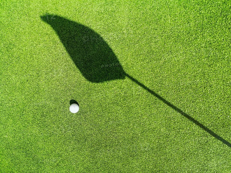 Golf ball on the green, shadow of a flag on a green, golf course