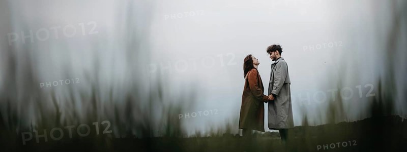 A couple standing apart in a field on an overcast day, holding hands, conveying a sense of connection