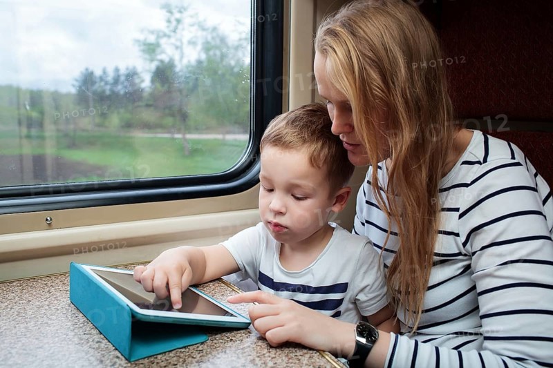 Mother and her little son using touchpad sitting by the window in the train