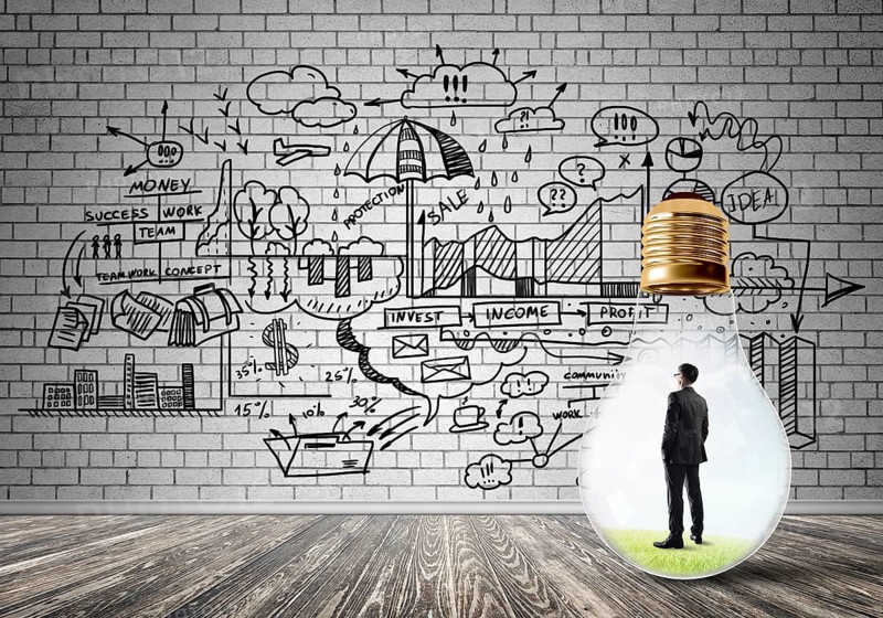 Businessman inside of light bulb in empty concrete room and sketches on wall