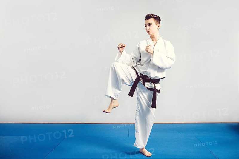 Girl in karate suit kimono in studio at grey background. Female child shows judo or karate stans in white uniform with black belt. Individual martial art sport . Full body portrait
