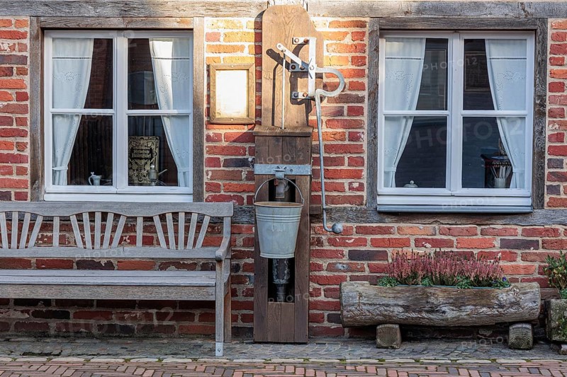 Rustic brick wall with two windows, old water pump and bench against a rural backdrop, gemen, münsterland, germany