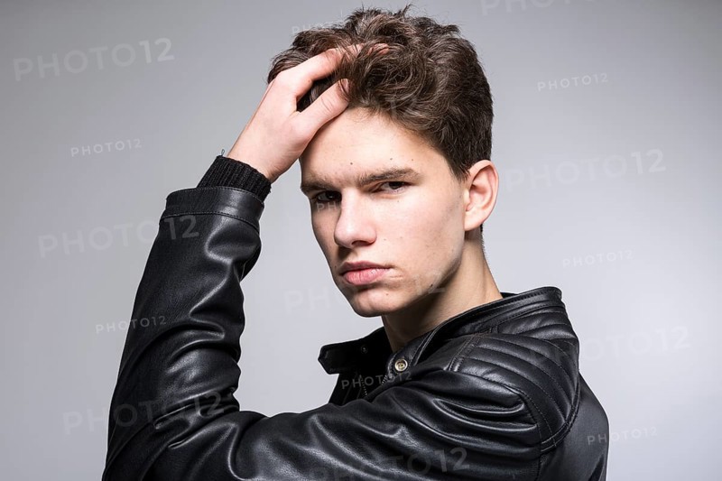 Young fashion man passing his hand through his hair. Male fashion model with hand in hair. Man Hair Beauty. Handsome Male Model Touching Healthy Hair. Stylish guy posing on grey background