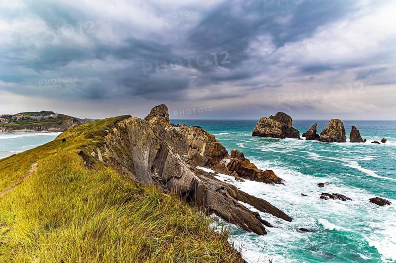 Rocky coastline of the Atlantic Ocean. Spanish coast, Cantabria. Portio beach. Stormy autumn day in the Bay of Biscay. Picturesque cliffs and huge stones oppose the ocean